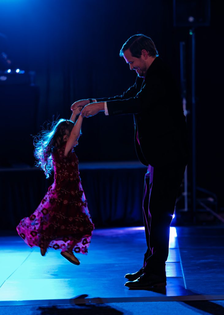 R5__0350-PR5 Photo of backlit father twirling young daughter through the air on dance floor